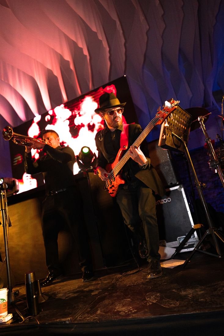Bajista y trompetista en escenario, cobertura de eventos
